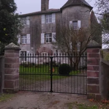 Portail en fer forgé noir avec piliers en pierre devant une demeure ancienne