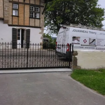 Portail coulissant en métal noir devant maison basque avec clôture assortie