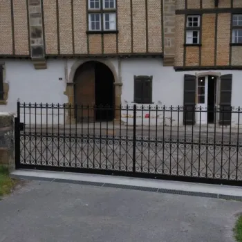 Portail en fer forgé noir sur rail, entrée de propriété avec façade traditionnelle