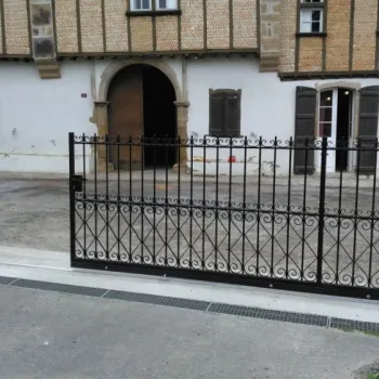 Portail en fer forgé décoratif noir avec motifs, installé devant une maison ancienne